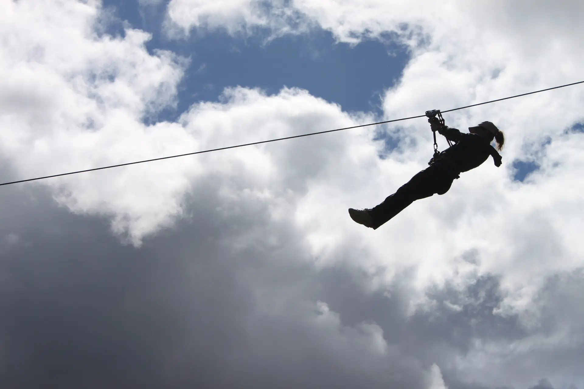 Ein Zipline-Fahrer als Silhouette vor Wolken, die Beine ausgestreckt, an einem WildPlay-Seil (Symbolbild, nicht die Niagara-Zipline)