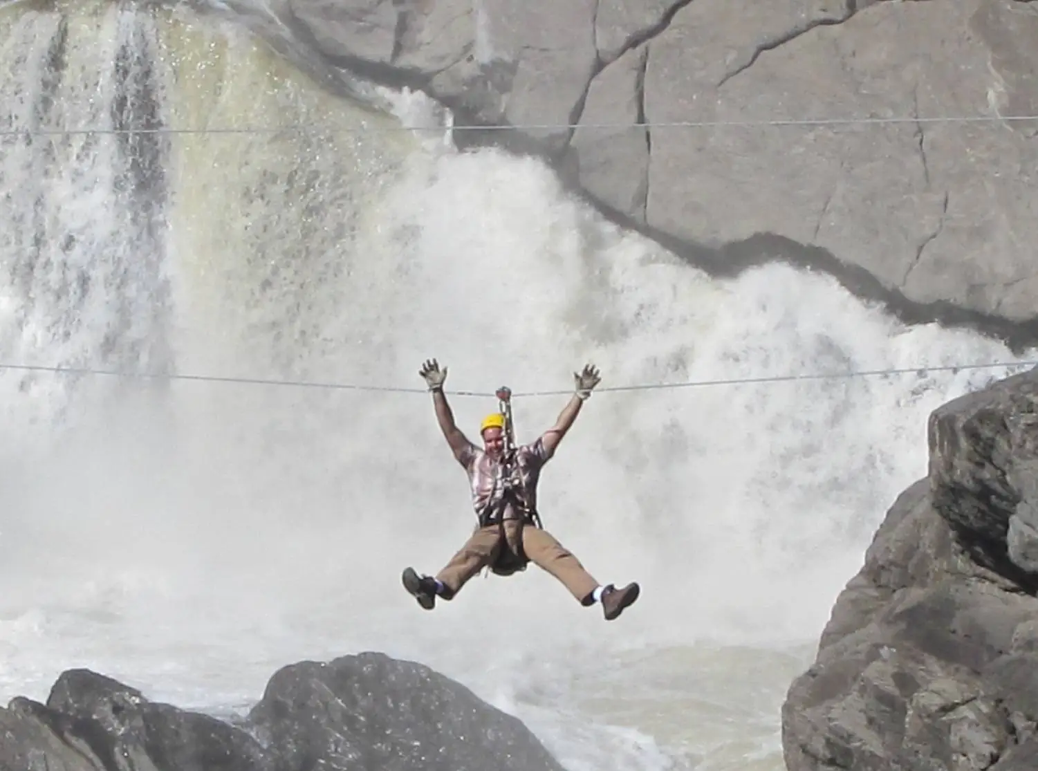 Ein Zipline-Fahrer mit ausgebreiteten Armen quert eine Schlucht vor einem tosenden Wasserfall (Symbolbild, Grand Falls, nicht die Cetina)